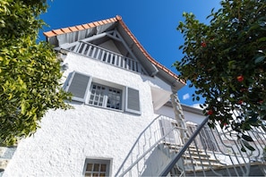 A white building with a red-tiled roof, a balcony, and a staircase.