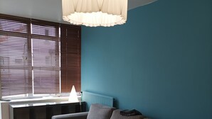 A living room with a grey sofa, a round wooden table, and a window with blinds. - Parisian apartment (Paris)