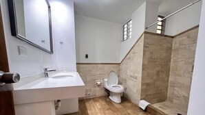 A bathroom with a white sink, a toilet, and a shower area with stone walls. - Apartamento DE 1 Dormitoio Alcanfores (Miraflores)