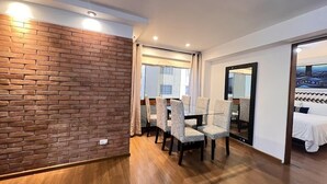 A modern room with a brick accent wall, wooden flooring, a dining area with patterned chairs, and a bed with a patterned bedspread. - Apartamento DE 1 Dormitoio Alcanfores (Miraflores)