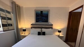 A hotel room with a large bed, two bedside lamps, a framed artwork above the bed, and a wooden door. - Apartamento DE 1 Dormitoio Alcanfores (Miraflores)