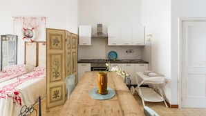 A compact kitchen with white cabinets, a stove, and a sink. A wooden table with a vase of flowers is in the center. - Villa Biancarosa - Rosa by BarbarHouse (Porto Cesareo)