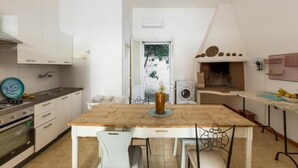 A kitchen with white cabinets, a wooden table, and a view of greenery outside. - Villa Biancarosa - Rosa by BarbarHouse (Porto Cesareo)