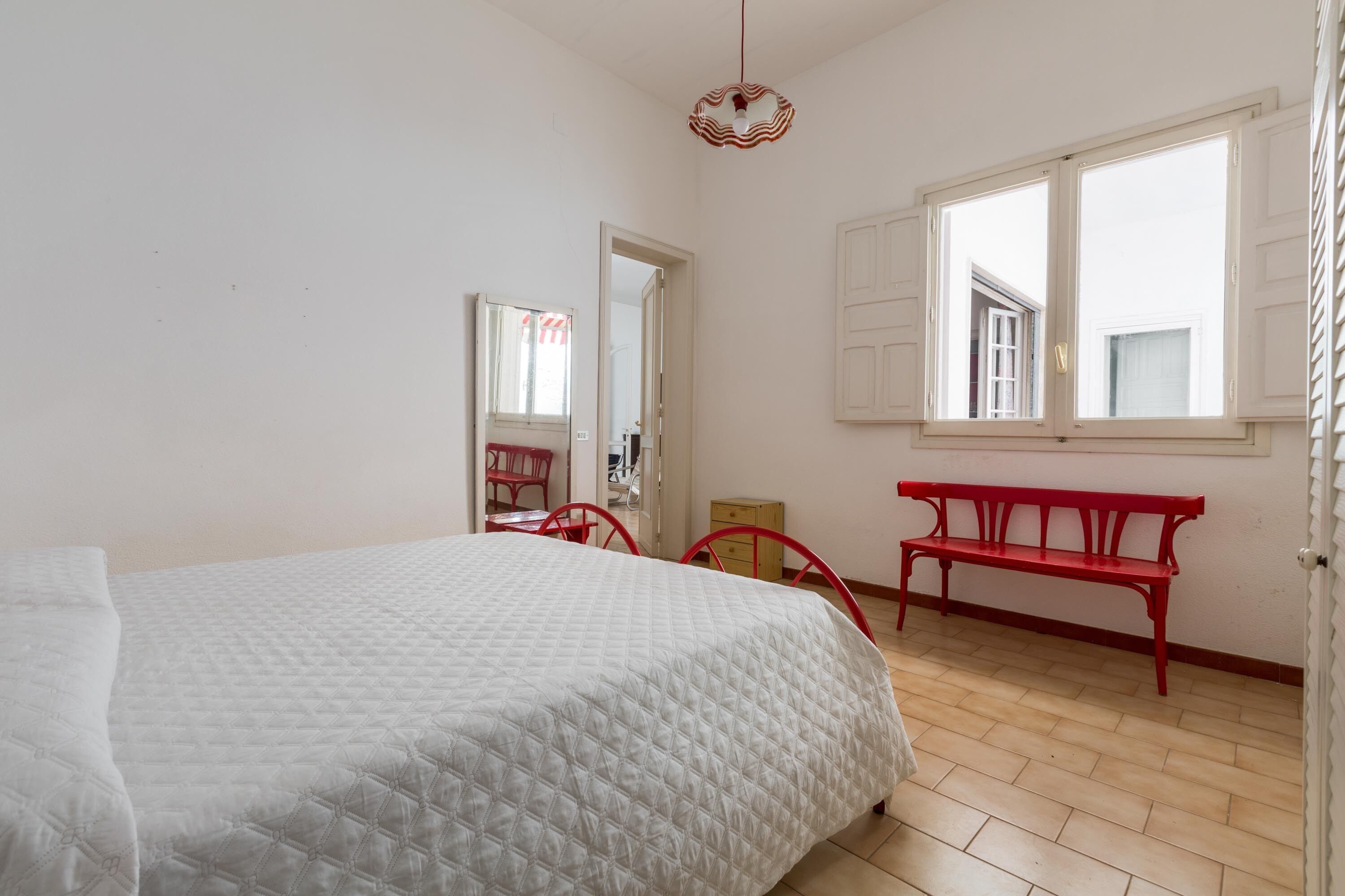 Ein Schlafzimmer mit einem Bett, einer roten Bank, einem Fenster und einem Spiegel.