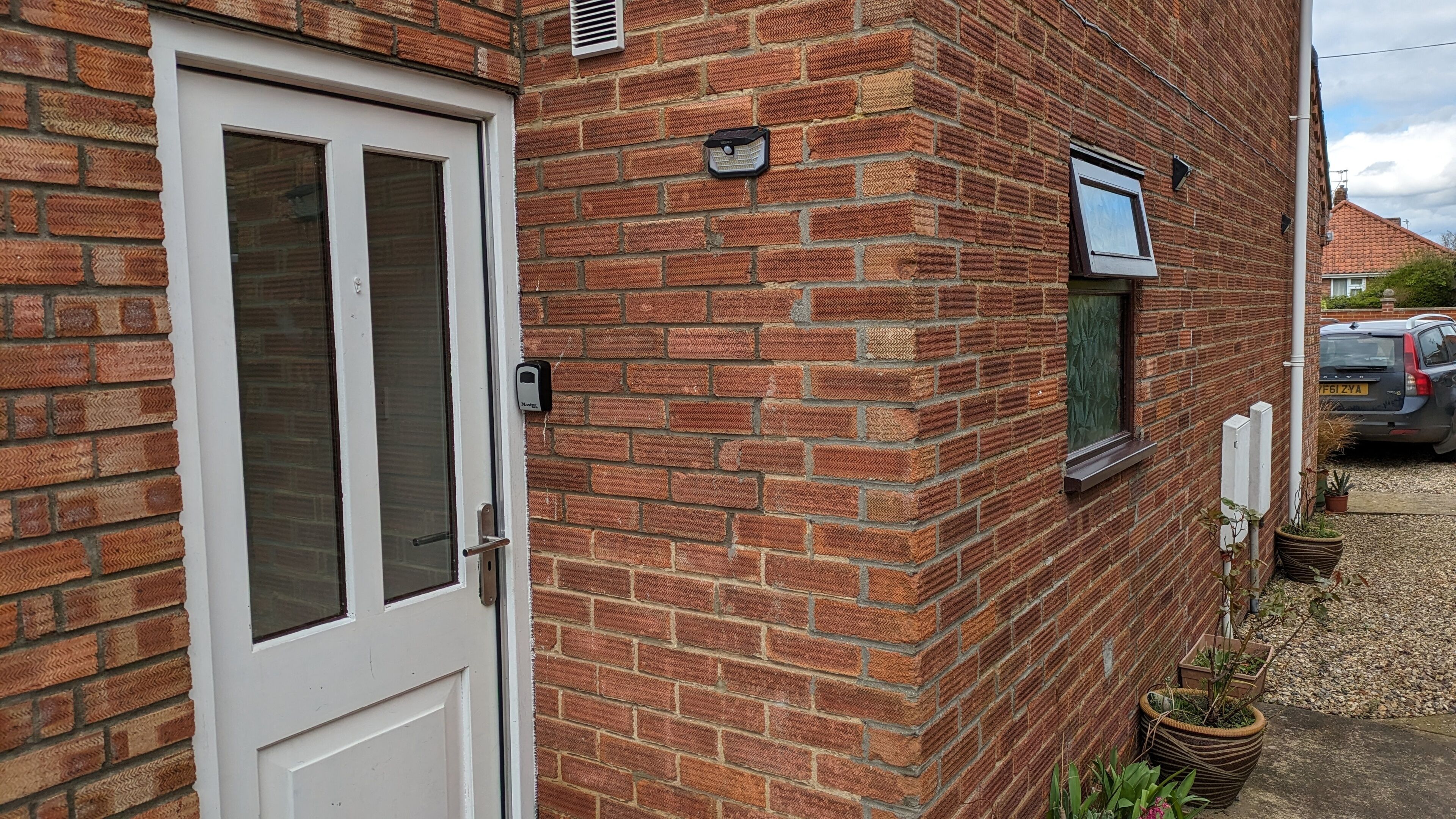 A brick house with a white door, a small window with a shutter, and a security device mounted on the wall.