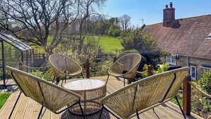 A deck with wicker furniture and a glass table, overlooking a green lawn and a brick house. - 3 bedroom accommodation in Calbourne (Calbourne)
