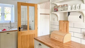 A kitchen with white cabinets, a wooden door, a window, a sink, and a shelf with jars. - 3 bedroom accommodation in Calbourne (Calbourne)