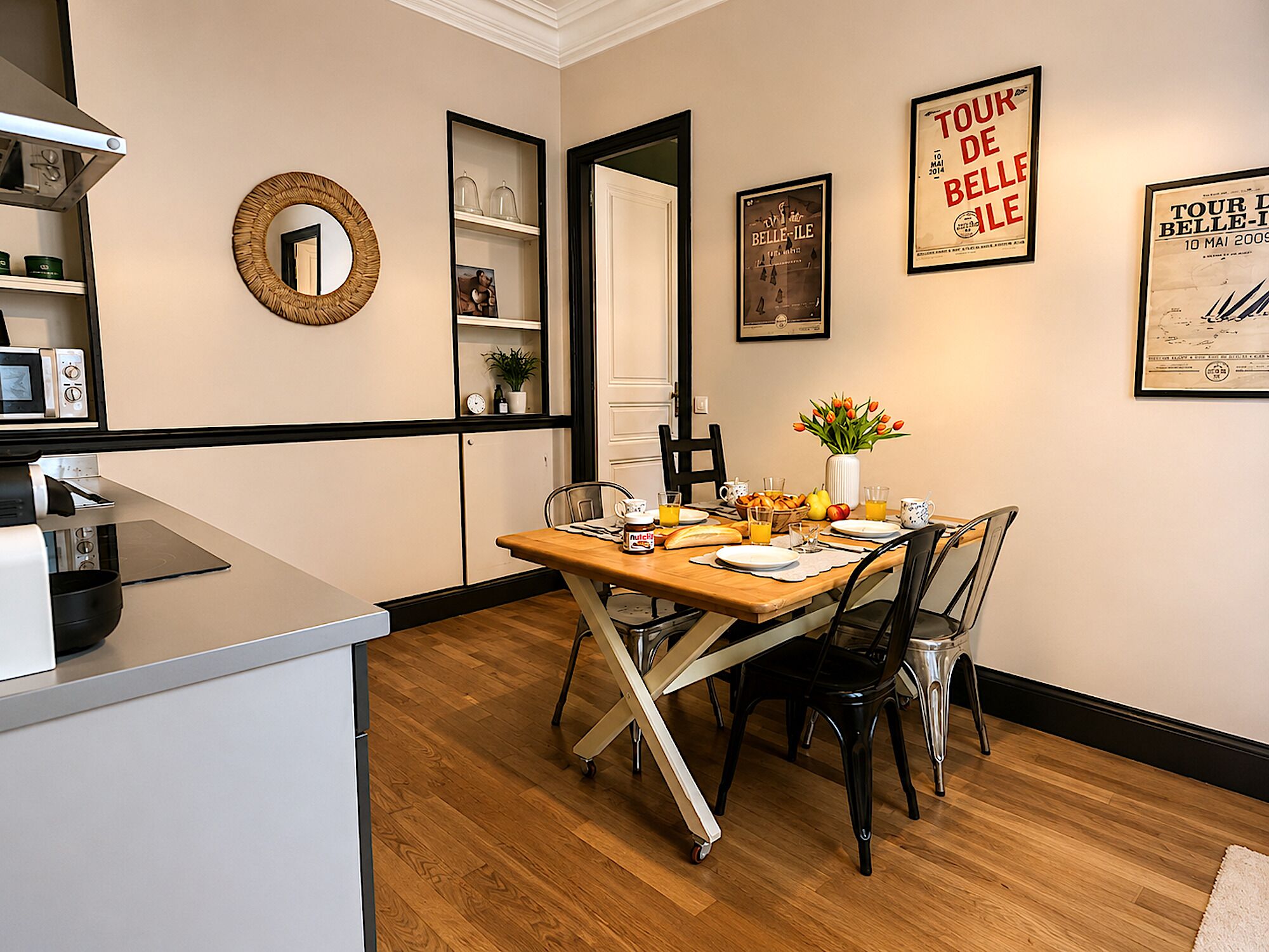 A dining area with a wooden table, chairs, a vase of flowers, and a wall with framed posters.