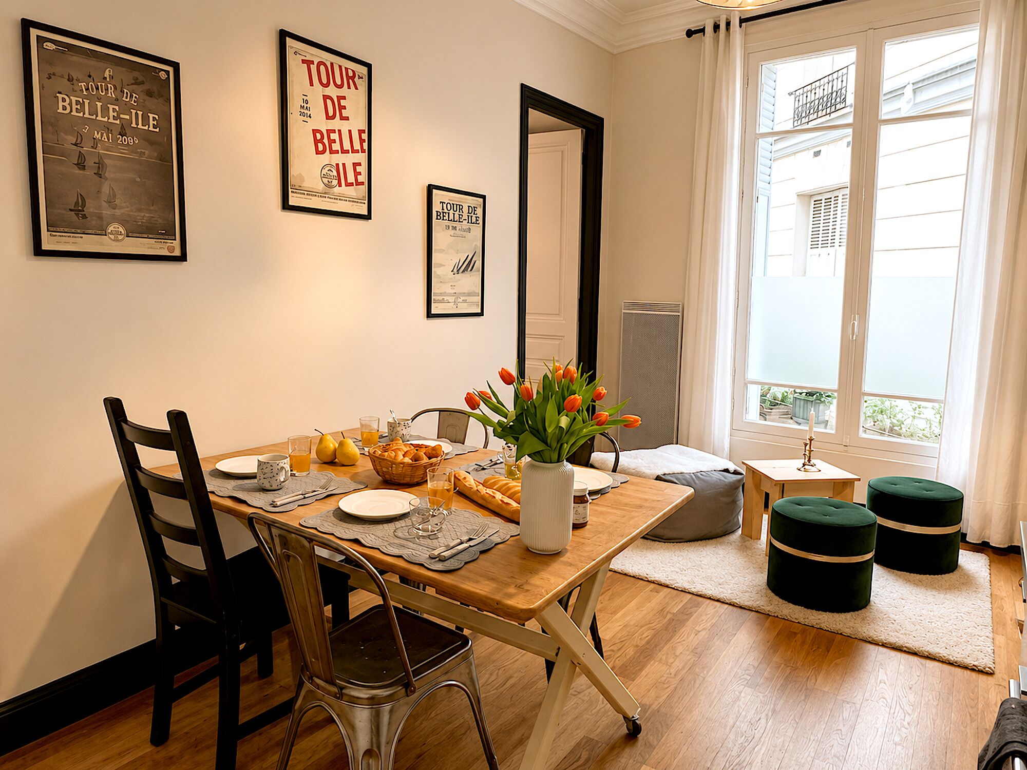 Un coin repas avec une table en bois, des chaises, un vase de tulipes et des affiches encadrées au mur.