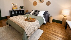 Et soveværelse med seng, natbord, lampe, billedvæg og et indrammet billede.