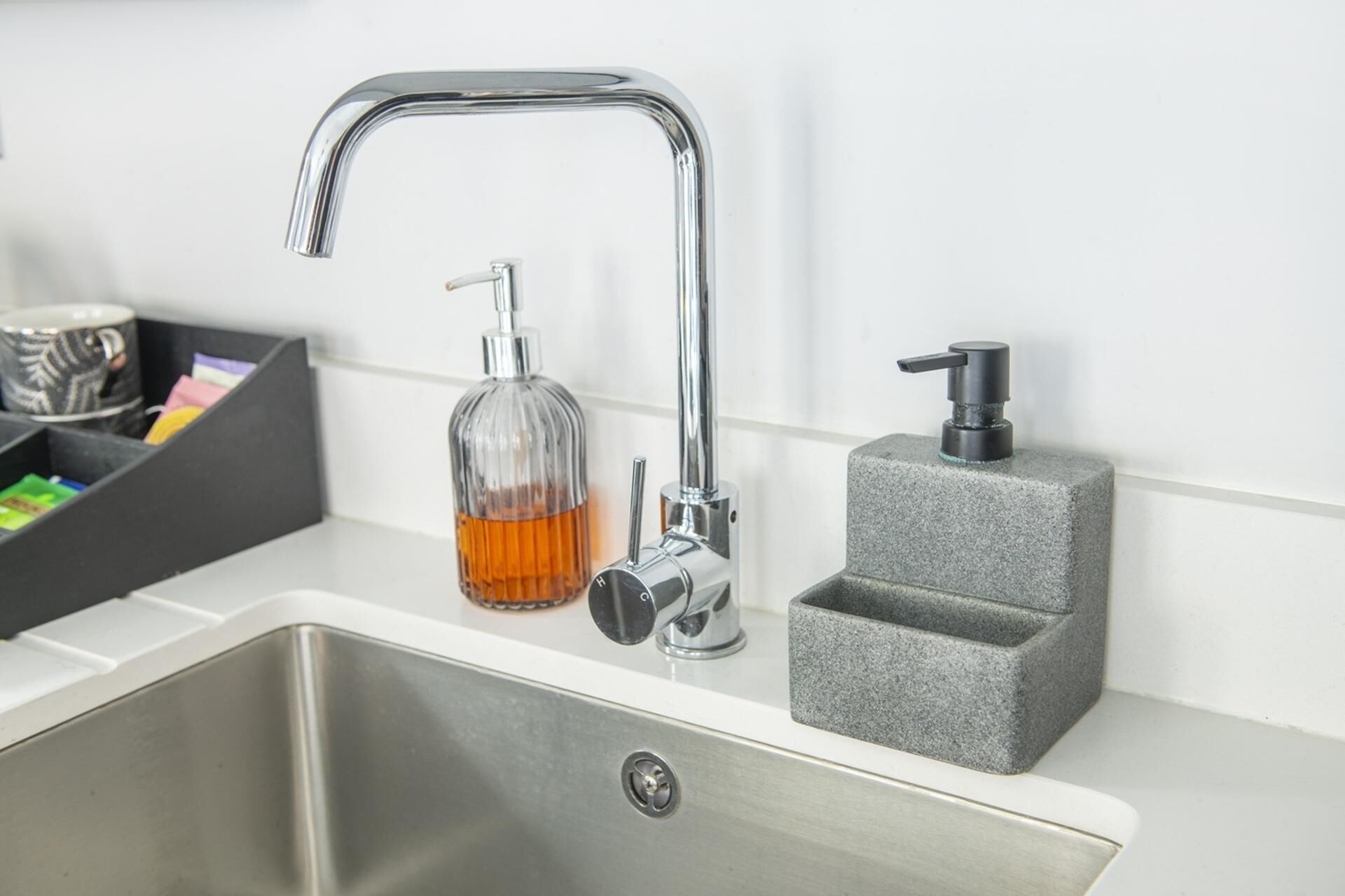 A stainless steel kitchen sink with a modern faucet, a soap dispenser, and a soap bottle.