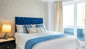 A hotel room with a large bed, a nightstand with a lamp, a view of the outdoors through a window, and a textured wall.