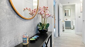 A hallway with a mirror, orchids, a bottle, and a tray with colorful bowls.