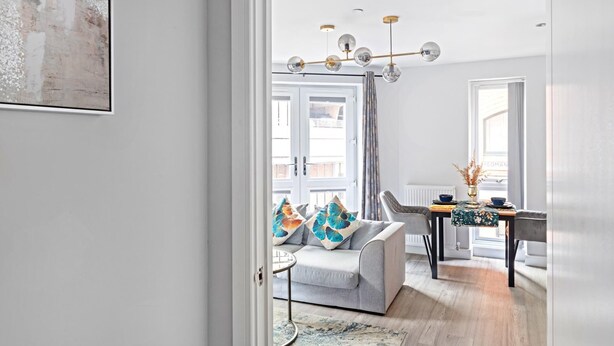 A modern living room with a grey sofa, a round coffee table, and a dining area with a table and chairs.