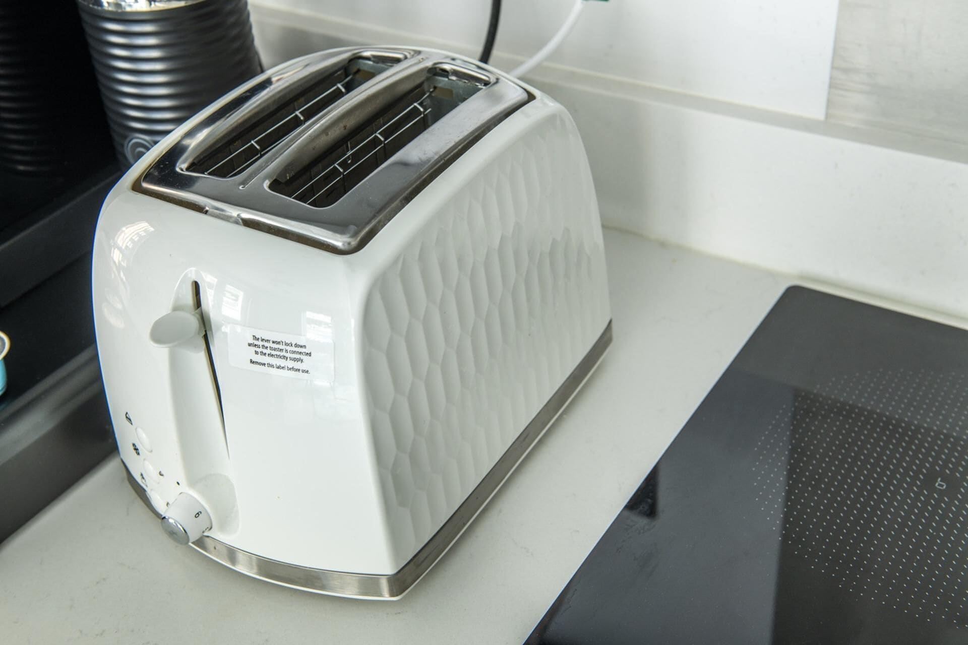 Un tostador blanco con una etiqueta en el lateral, situado sobre una encimera de cocina junto a un electrodoméstico negro.