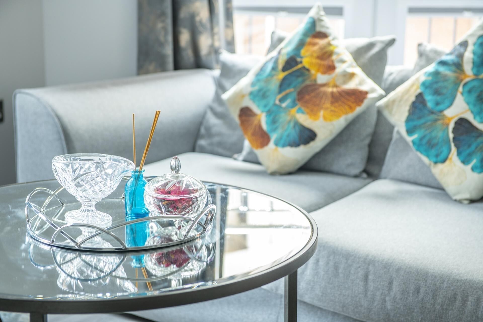 A glass table with a crystal bowl, a blue vase, and a glass container with sticks.