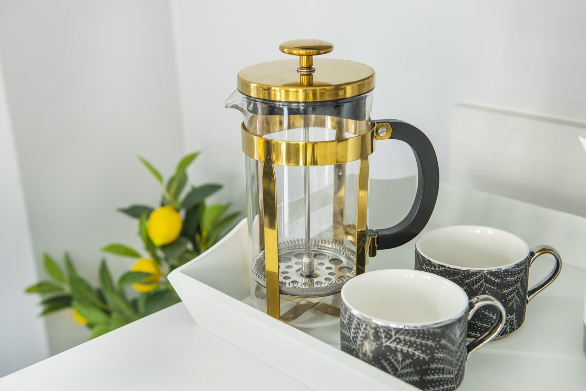 A French press coffee maker on a tray with two patterned mugs.