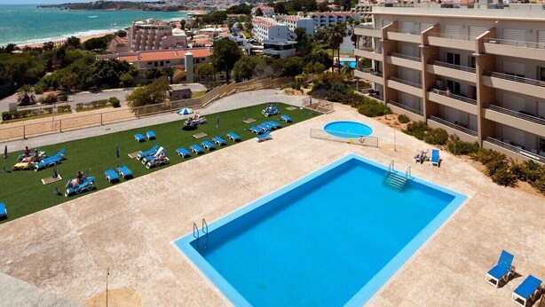 A hotel with a large pool, sun loungers, and a view of the beach.
