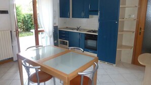 A compact kitchen with blue cabinets, a gas stove, and a sink. There is a dining table with four chairs. - Holiday apartment mit Pool (Cavallino-Treporti)