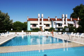 Una piscina con sillones de descanso y un edificio con techo rojo al fondo.