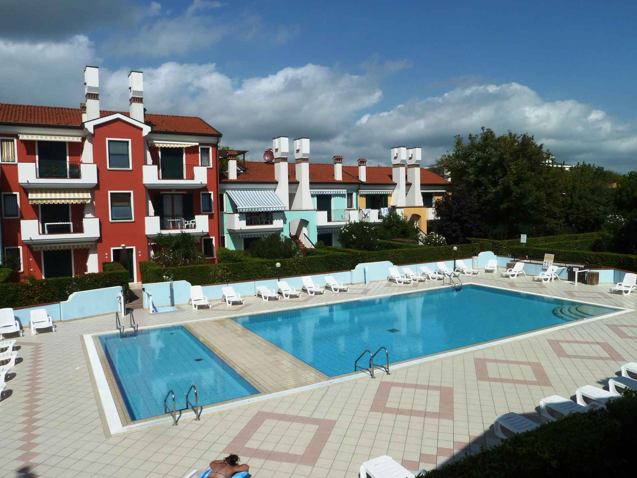 Una piscina con lettini e un edificio sullo sfondo con numerosi balconi.