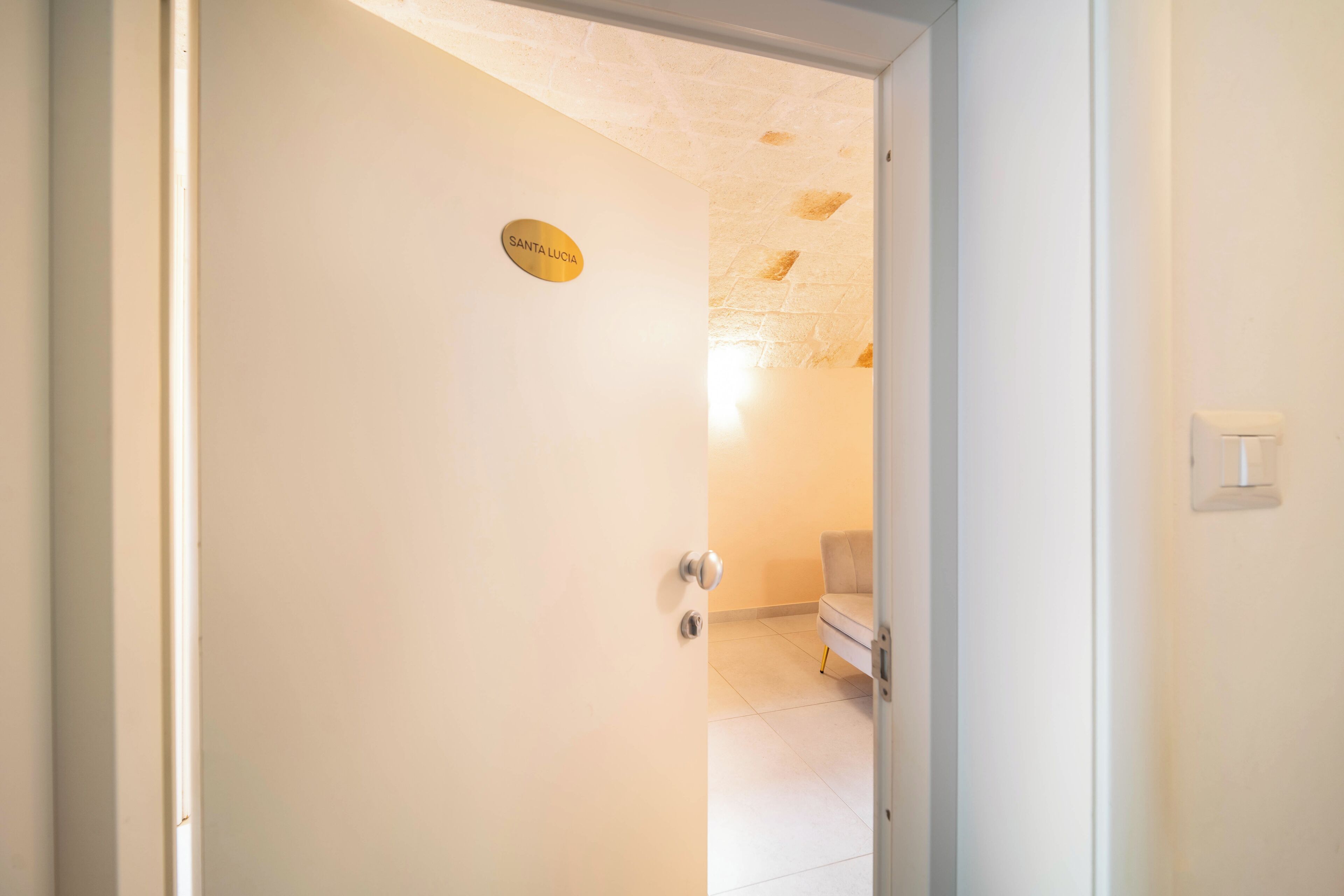 A door with a sign reading 'SANTA LUCIA' leading into a room with a white wall and a ceiling with exposed stonework.