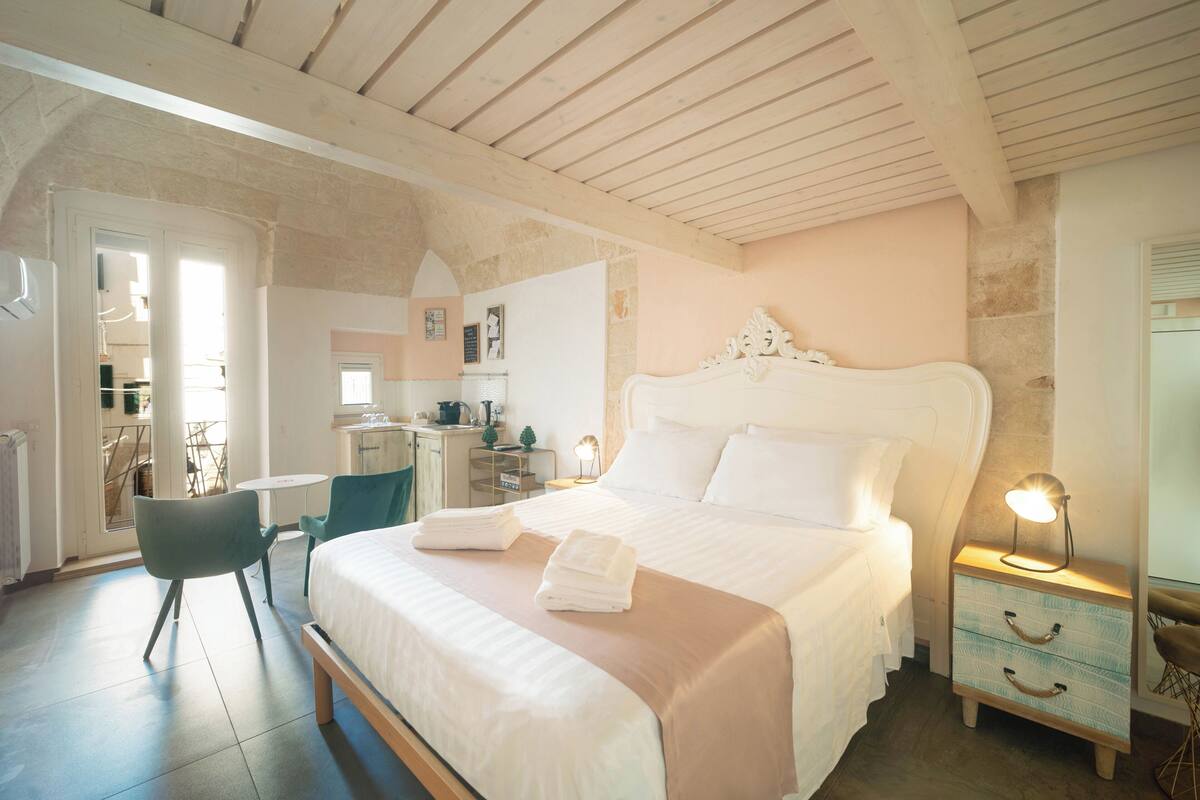 A bedroom with a large bed, bedside tables, a chair, and a desk with a lamp.