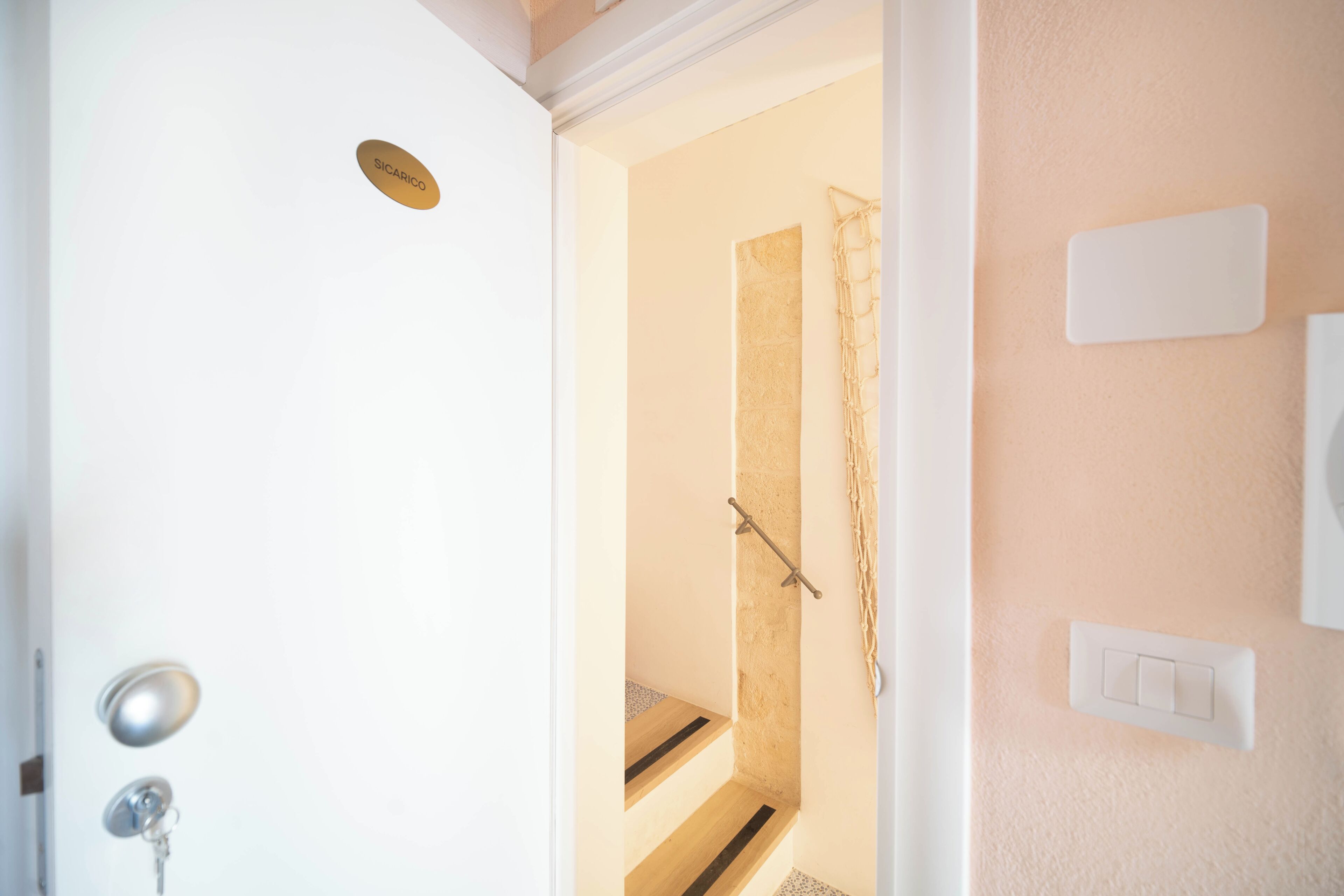 Una habitación de hotel con una puerta blanca, un ojo de cerradura, un interruptor de luz y una pequeña placa en la pared.