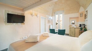A hotel room with a bed, a TV mounted on the wall, a kitchenette, and a view of the outside. - Le Contrade Chiasso Cafaro (Monopoli)