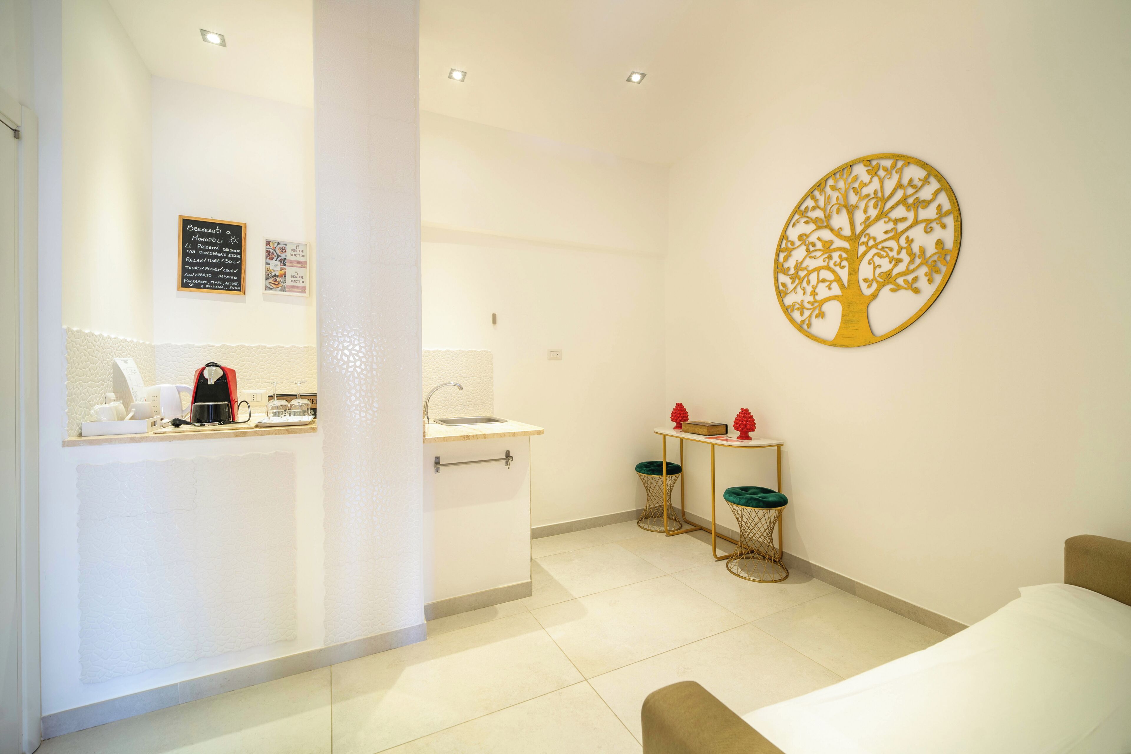 A modern hotel room with a bed, a small table with chairs, a sink, and a decorative tree wall art.