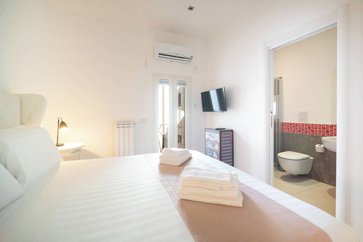 A hotel room with a bed, a TV, a bathroom with a toilet and sink, and a door leading to another room.