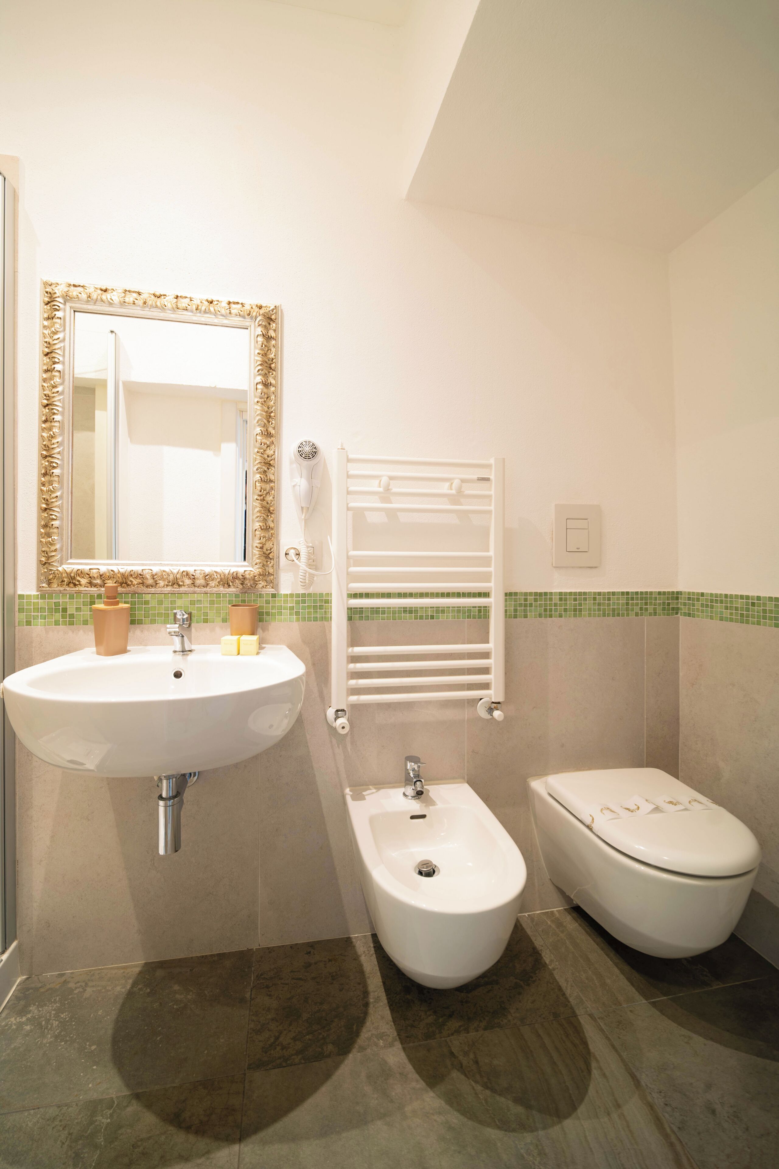 A bathroom with a sink, bidet, toilet, and a mirror with an ornate frame.