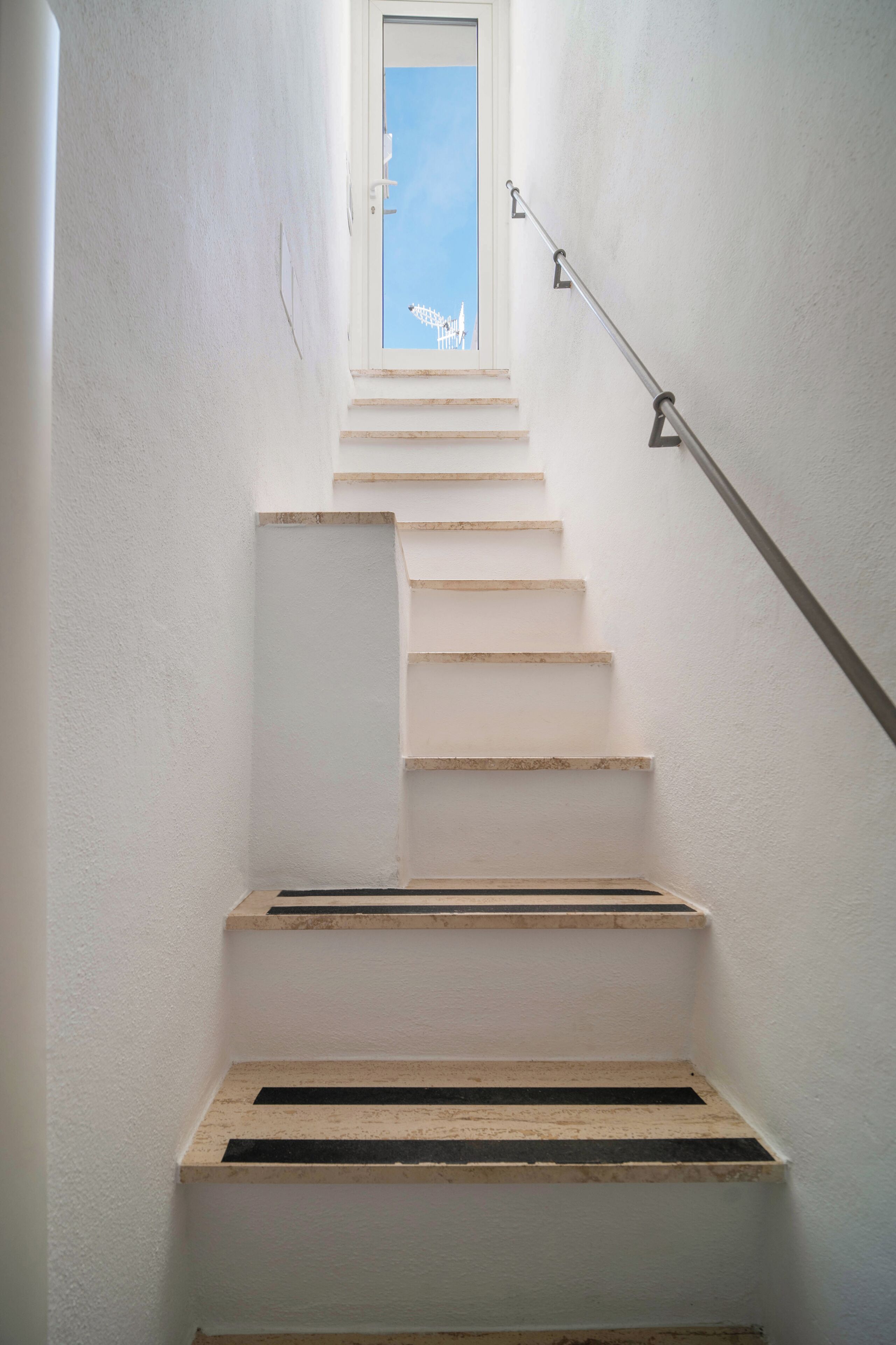 Un escalier offrant une vue sur les toits d’une ville, à travers une fenêtre.