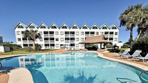 A swimming pool with lounge chairs and a building with a distinctive roofline in the background. - Gulf Shores Plantation IV (Gulf Shores)