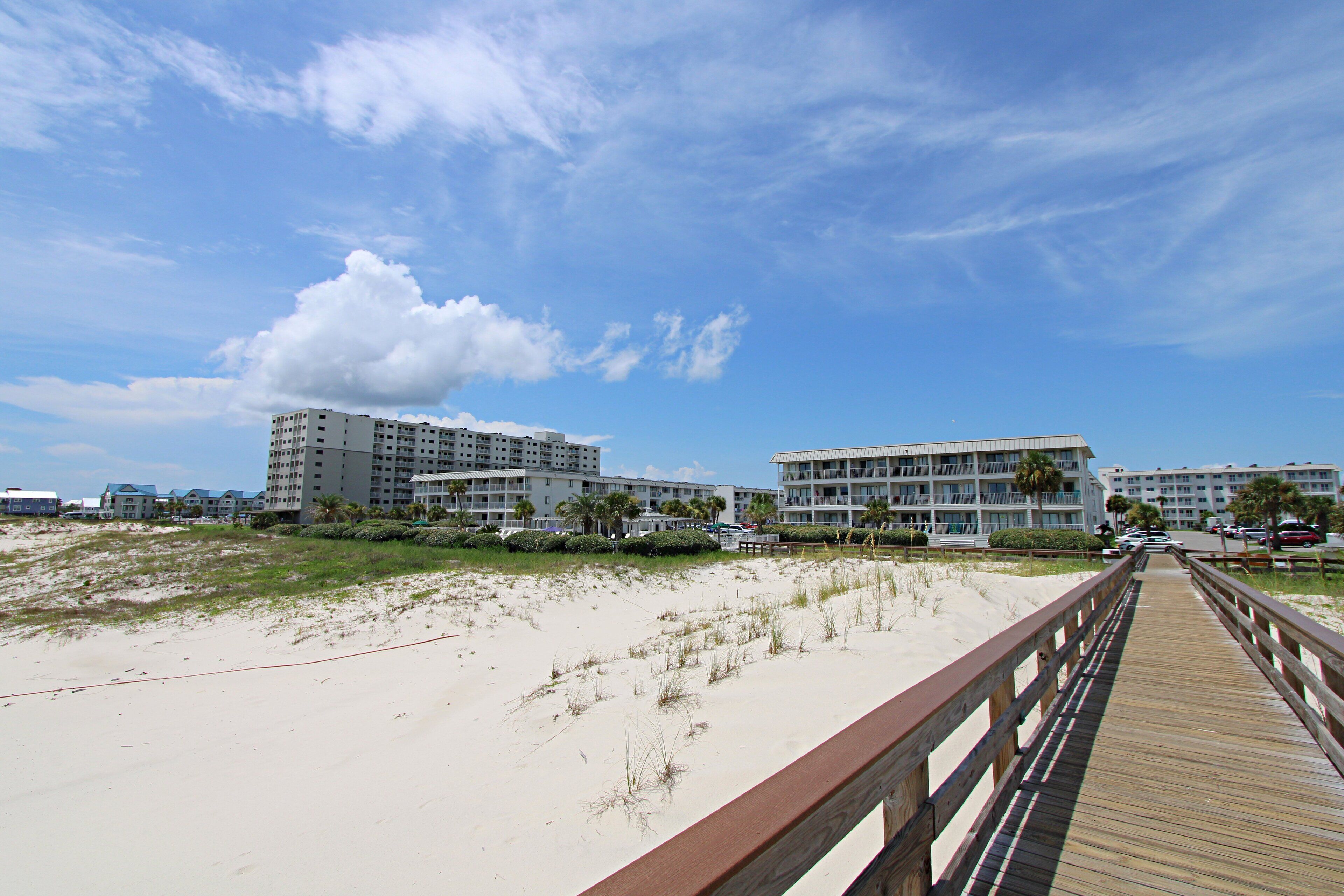 Un paseo marítimo a la orilla de la playa que conduce a hoteles frente al mar, con varios pisos y balcones.