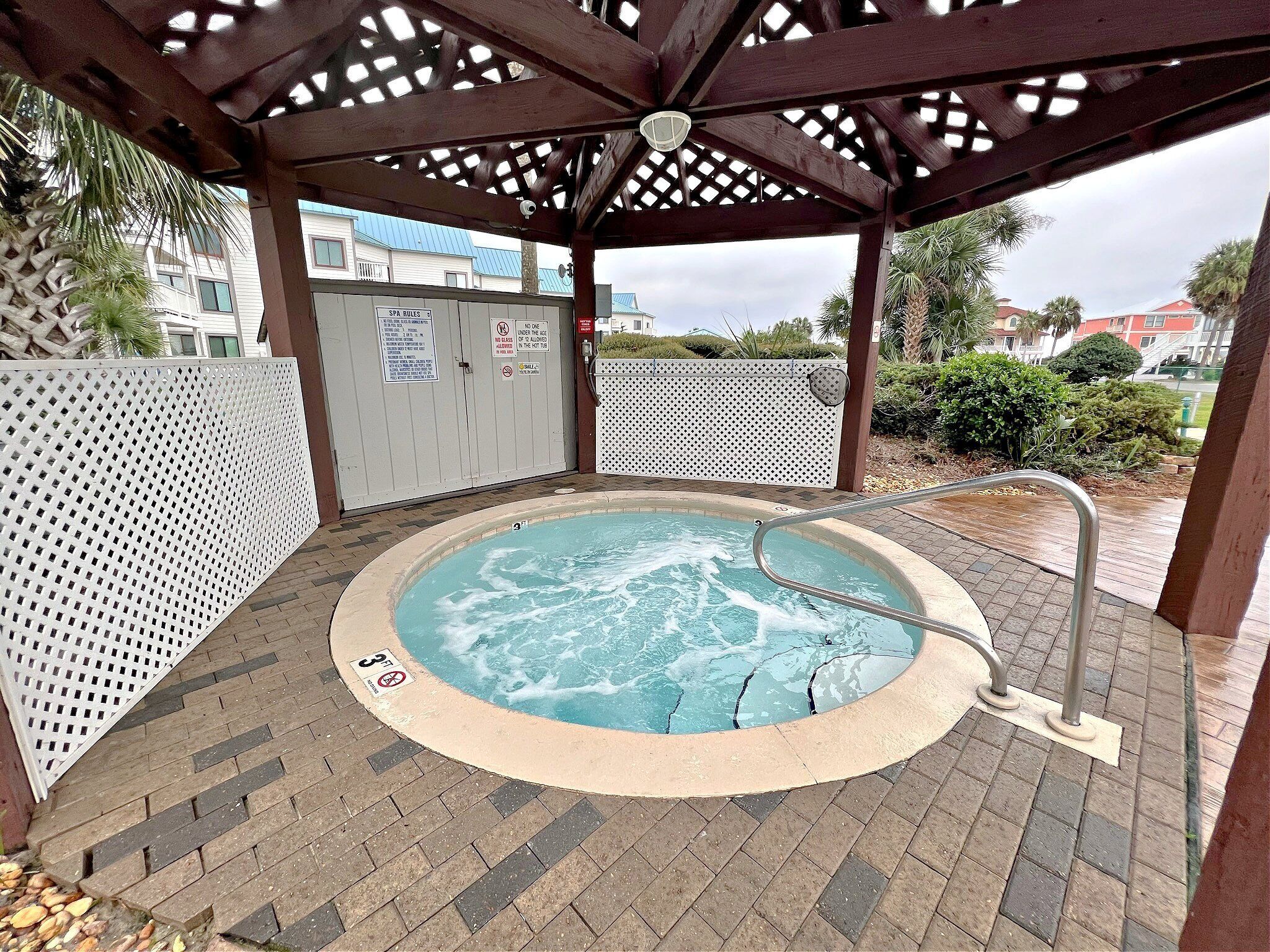 A hot tub area with a wooden pergola overhead, a pool with a 3ft depth marker, and a white fence with spa rules signs.