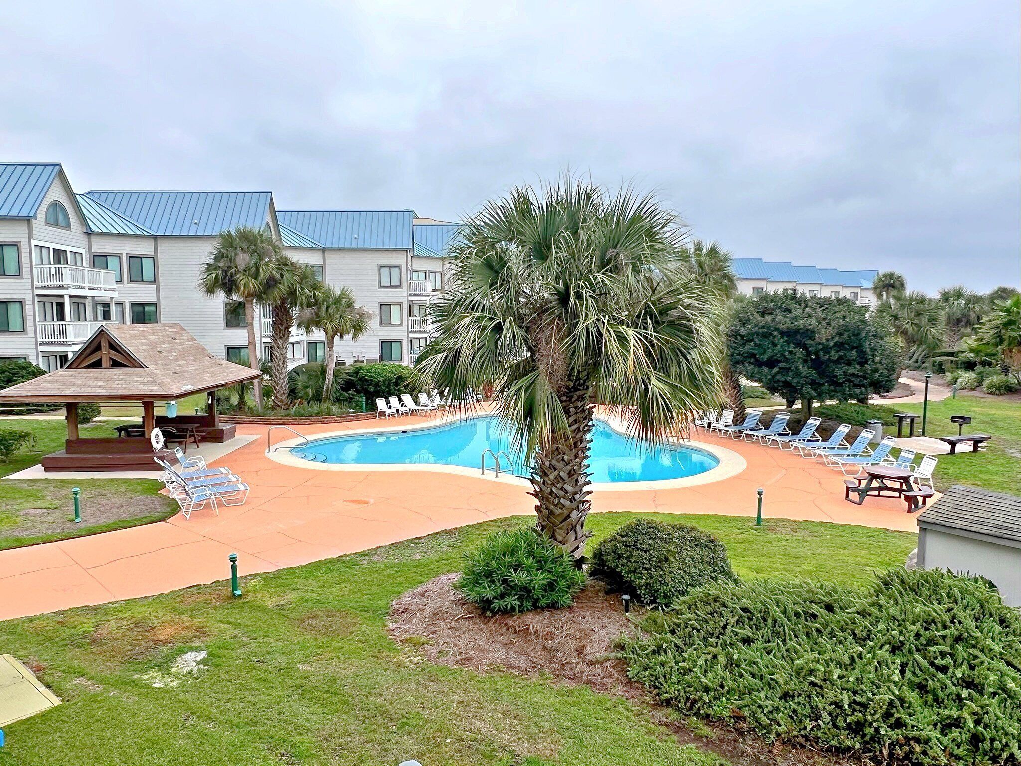 Ein Swimmingpool mit Liegestühlen, einer Laube und einem Gebäude mit blauem Dach im Hintergrund.