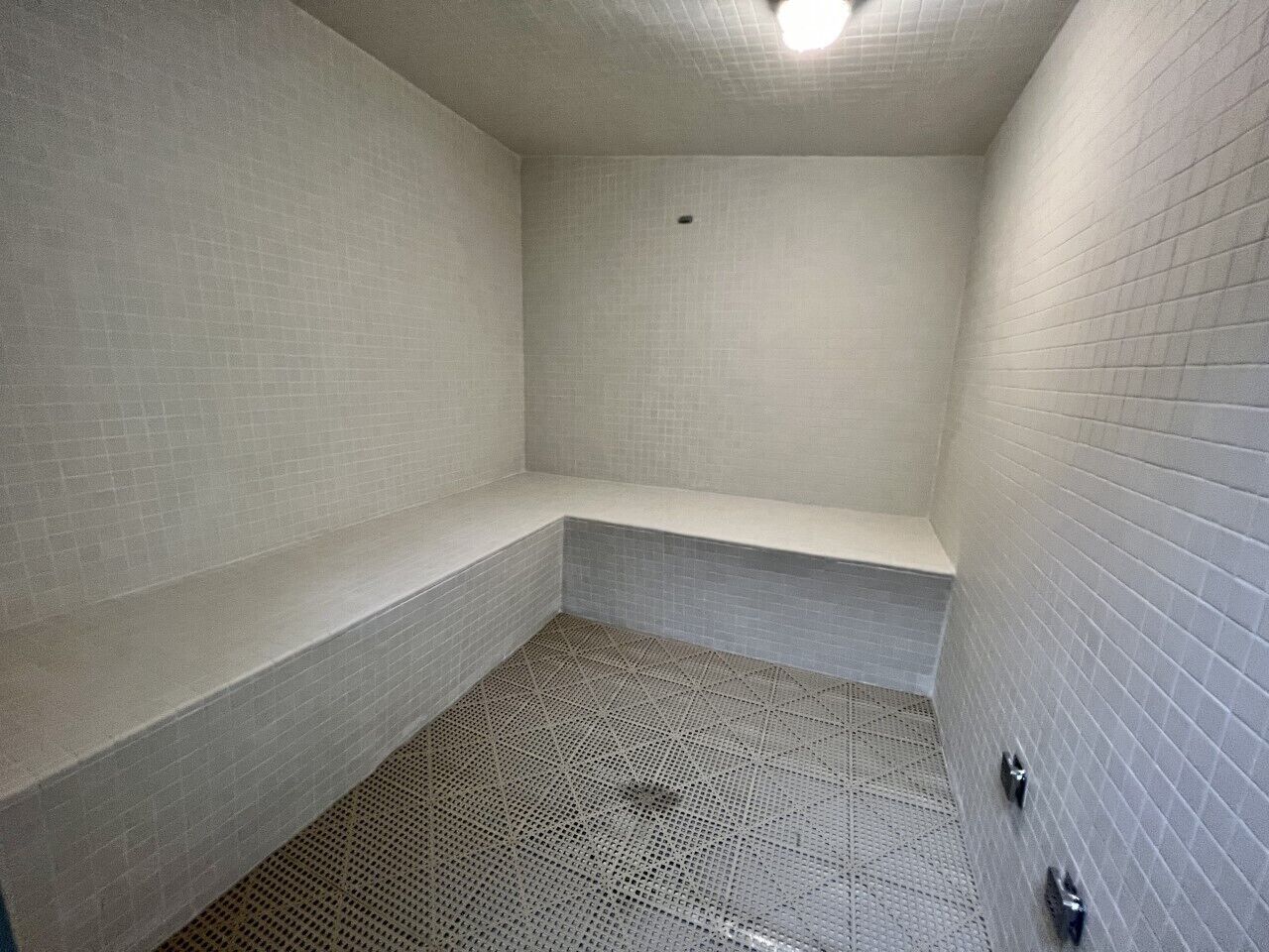 A small, enclosed bathroom with tiled walls and floor, a bench, and a shower area.