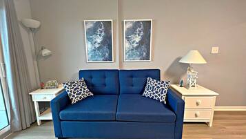 A blue sofa with patterned cushions, a white nightstand with a lamp, and two framed pictures on the wall.