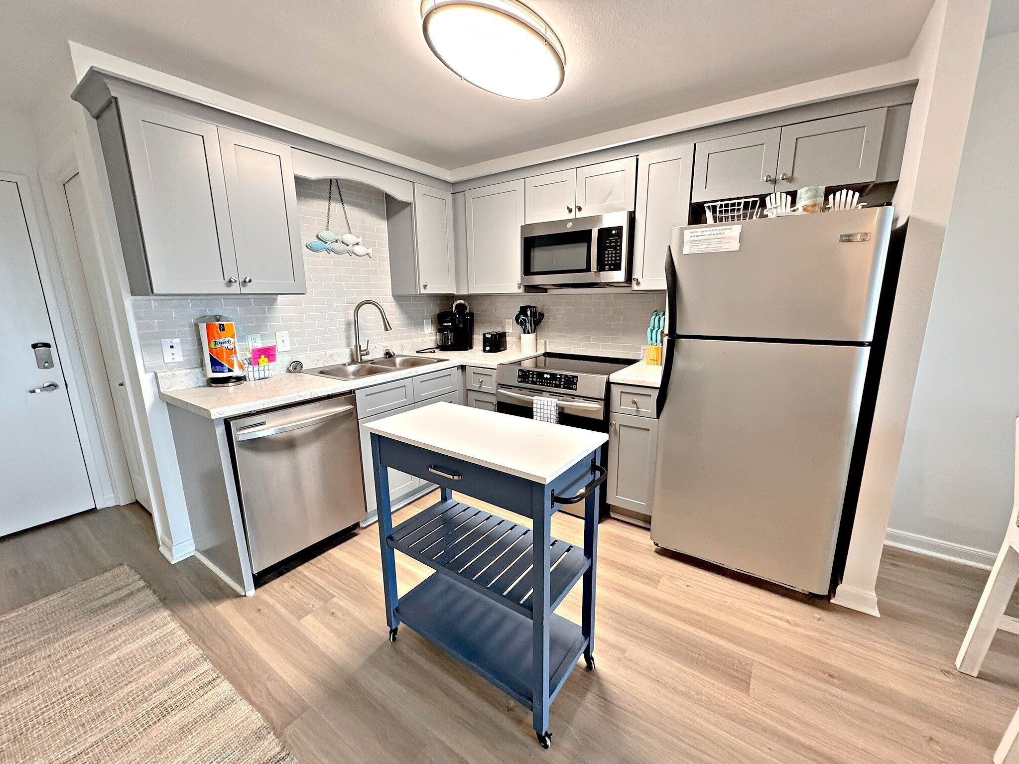 A modern kitchen with white cabinets, stainless steel appliances, and a blue cart.
