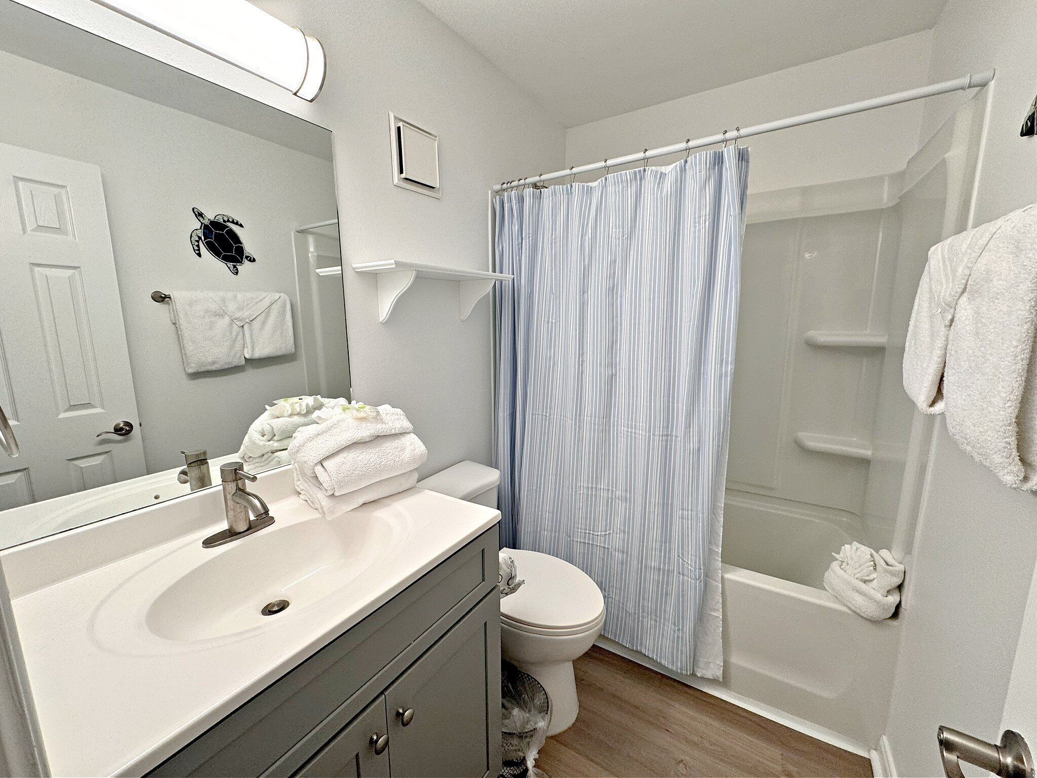 Een badkamer met een wit wastafel, een spiegel, toilet, douchegordijn en een handdoekrek.