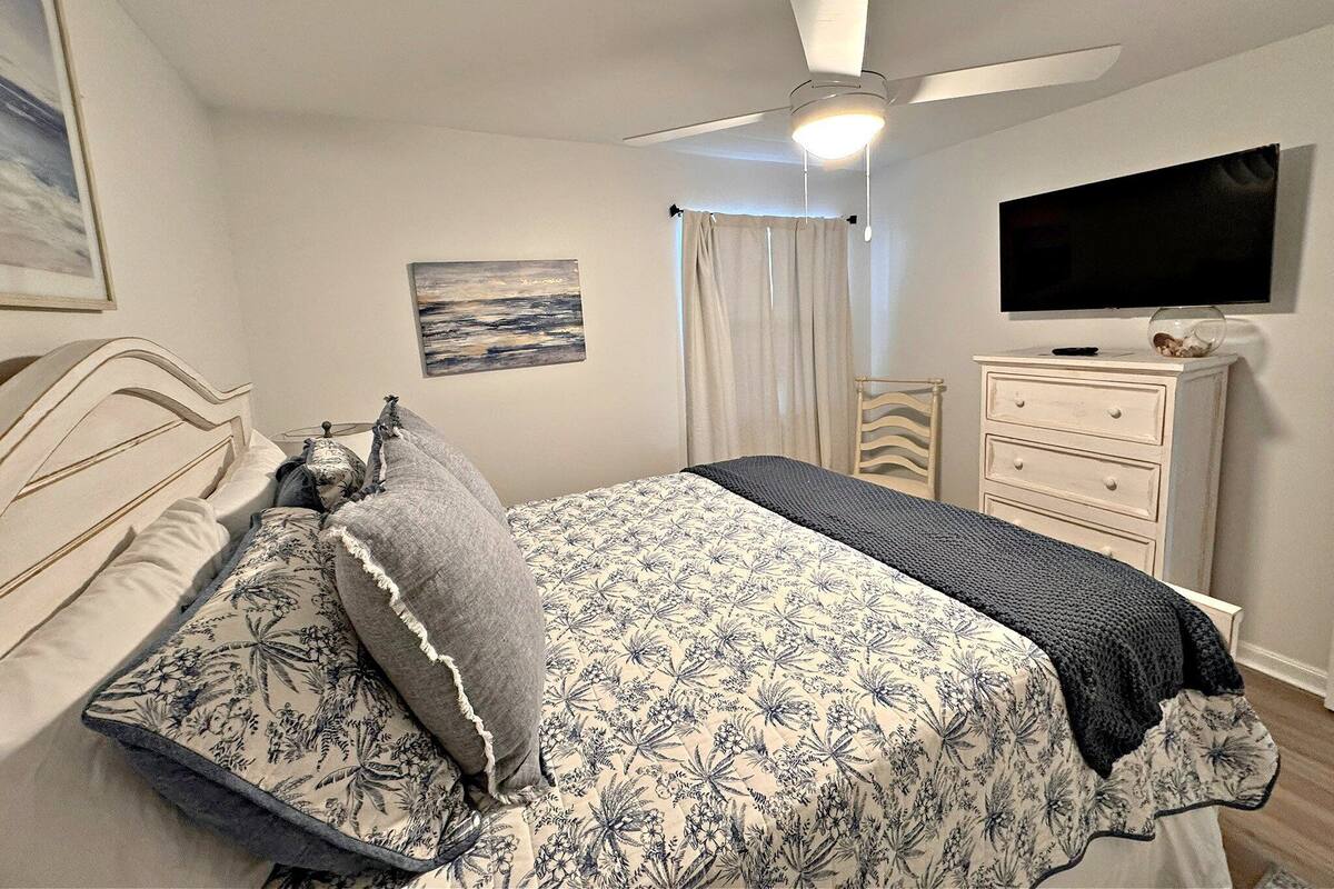 Un dormitorio con cama, cómoda, televisor y ventilador de techo.