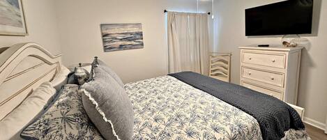 A bedroom with a bed, a ceiling fan, a TV, a dresser, and a painting on the wall.