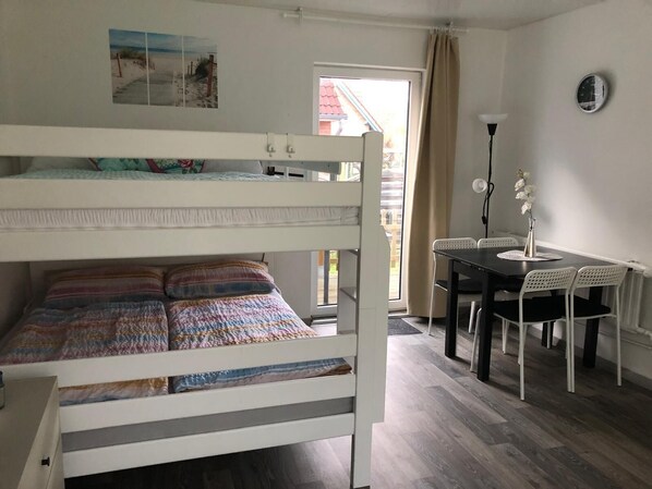 Un lit superposé avec une couverture aux couleurs vives, une table à manger avec des chaises, une lampe et une horloge au mur.