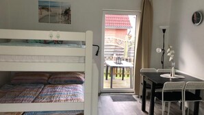Een kamer met een stapelbed, een eettafel met stoelen, een vaas met bloemen en uitzicht op buiten.