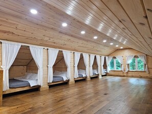 A cabin with wooden floors, multiple beds with white curtains, and a sloped ceiling with recessed lighting.