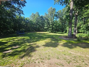 Vehreä ulkoalue, jossa on puita, trampoliini ja keinuteline.
