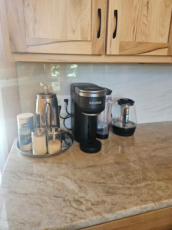 A kitchen with a Keurig coffee maker, a N'Joy coffee creamer can, a glass jar, and a coffee pot on a marble countertop. - Cozy 4-bedroom cabin in beautiful Gobles with AC and charm (Gobles)