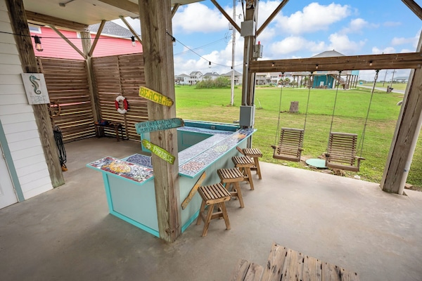 Tiki bar area with bar stools, wooden swings, hammocks, & 2 large picnic tables