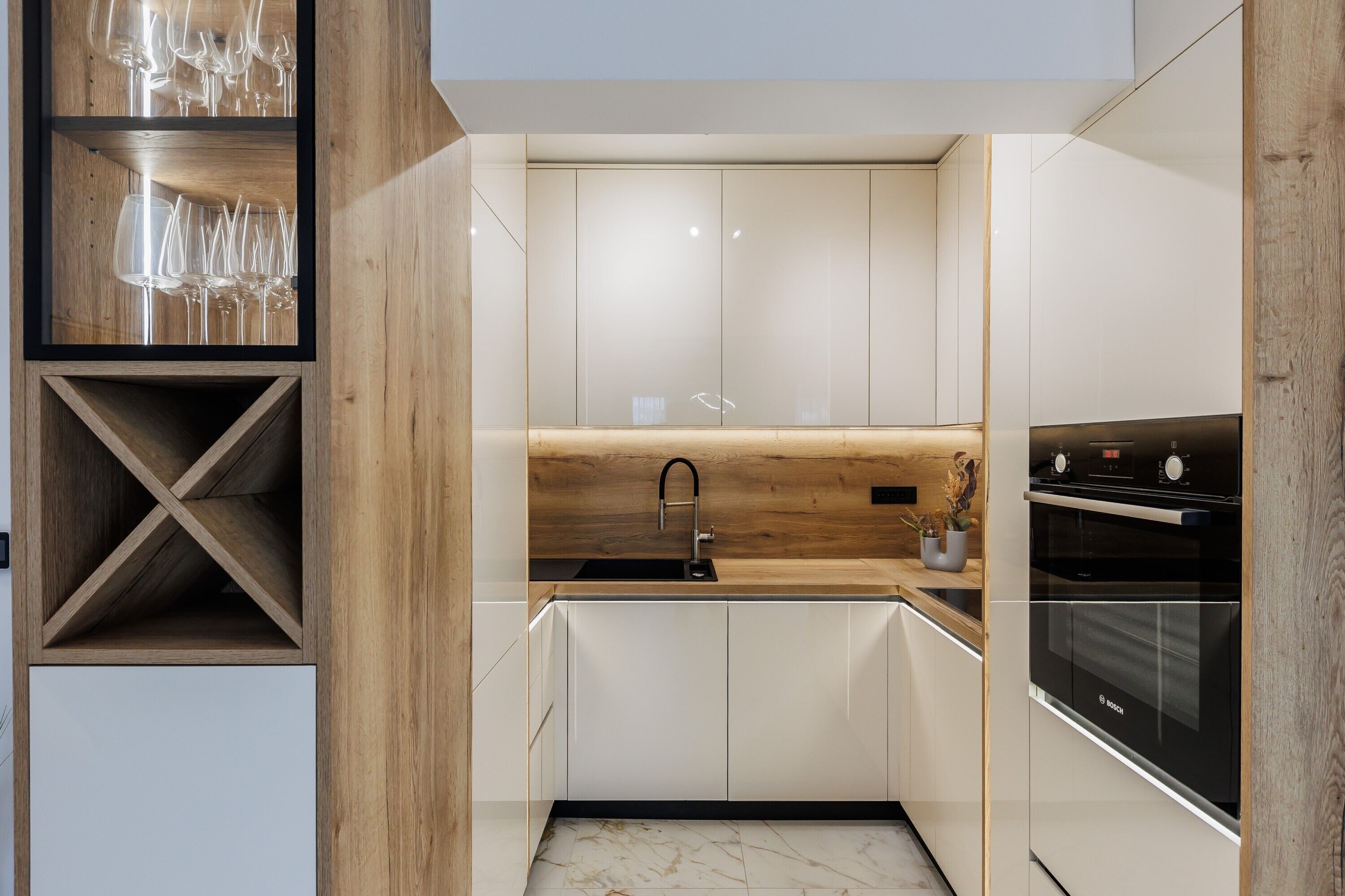 A modern kitchen with white cabinets, a wooden countertop, a Bosch oven, and a wine rack with glasses.